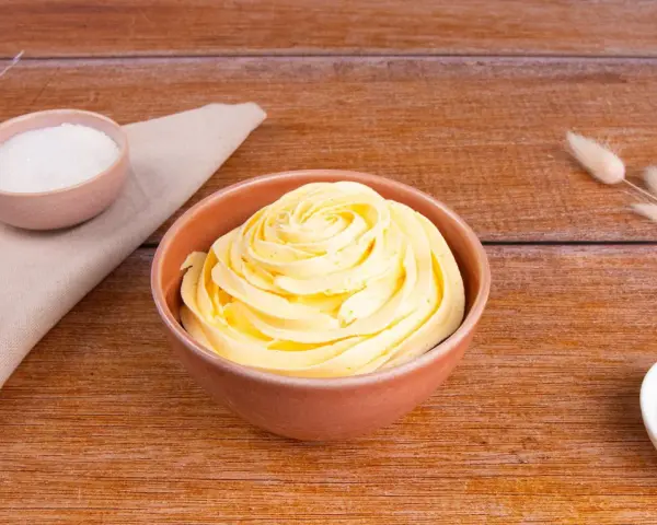 Crema al burro ricetta della nonna, soffice e profumata, pronta per decorare torte. Zucchero e ingredienti in vista.