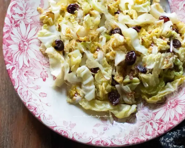 Deliziosa insalata di verza con uvetta, servita su un piatto decorato con fiori rossi.