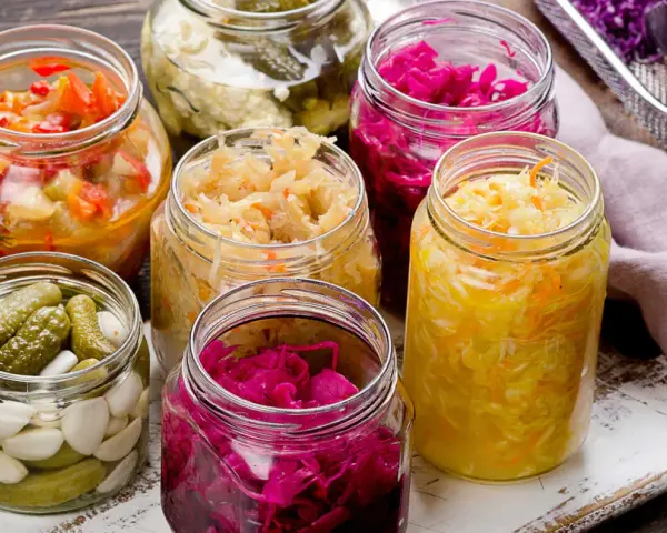 Vasi di vetro pieni di cibi fermentati fatti in casa: crauti, cavolo rosso, cetriolini e verdure miste.