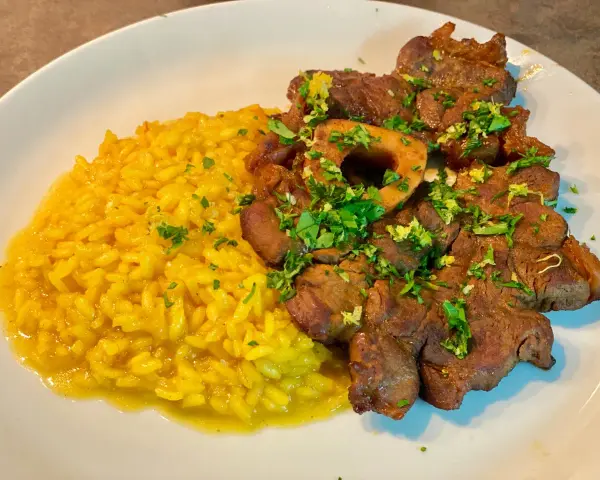 Un piatto invitante di risotto giallo cremoso accanto a un ossobuco tenero, guarnito con prezzemolo fresco e scorza di limone.