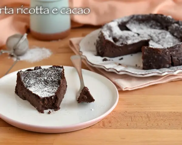 Una fetta di torta ricotta e cioccolato senza farina, cosparsa di zucchero a velo, su un piatto bianco.