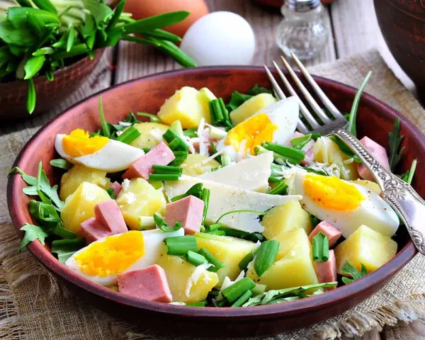 Deliziosa insalata di patate estiva con uova sode, salumi, formaggio e erbe fresche, servita in una ciotola di terracotta.