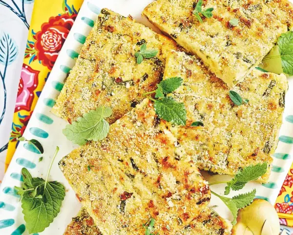 Fette dorate di polpettone di fagiolini, guarnite con erbe aromatiche fresche, su un piatto decorato con motivi floreali vivaci.