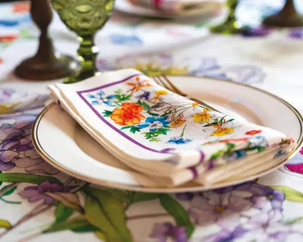 Tovagliolo fiorito piegato su un piatto bianco, con un bordo dorato. La tovaglia è decorata con un motivo floreale vivace. Il tovagliolo va a destra o sinistra?