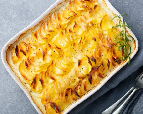 Delizioso millefoglie di patate dorate e croccanti, cotto in una teglia bianca, guarnito con rosmarino fresco e pepe nero.