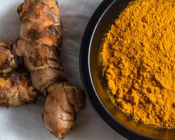 Radici di curcuma e polvere dorata in una ciotola, perfette per dare colore e sapore alla pasta.