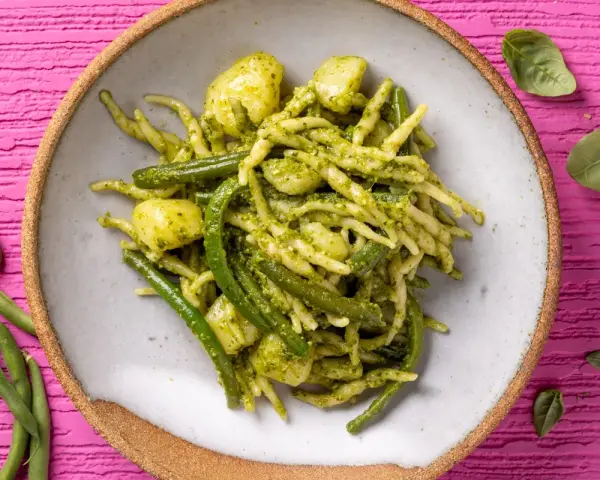 Un piatto invitante di trofie al pesto, con fagiolini e patate, su uno sfondo rosa vibrante.