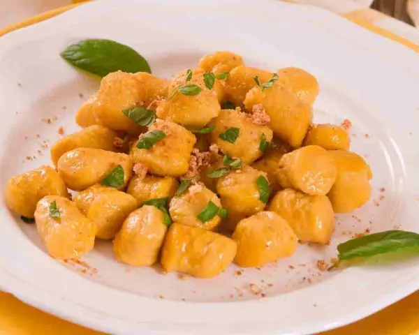 Gnocchi di zucca dorati e soffici, guarniti con basilico fresco e una spolverata di pangrattato croccante, serviti su un piatto bianco.