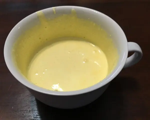 Una tazza bianca contiene un composto giallo pallido, un uovo sbattuto con zucchero, pronto per essere cucinato.