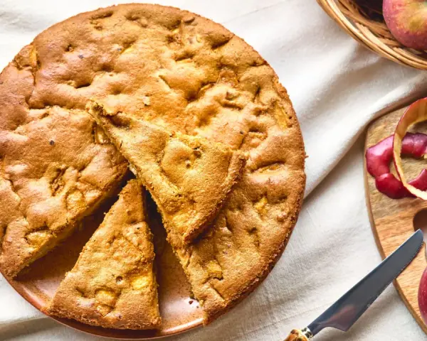 Una deliziosa torta di mele con farina di avena, appena sfornata, con mele fresche e scorze su un tagliere.