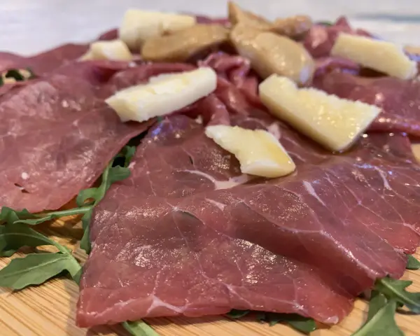 Carne salada cos'è? Fettine sottili di carne rossa, condite con erbe aromatiche e scaglie di formaggio stagionato, su un letto di rucola fresca.