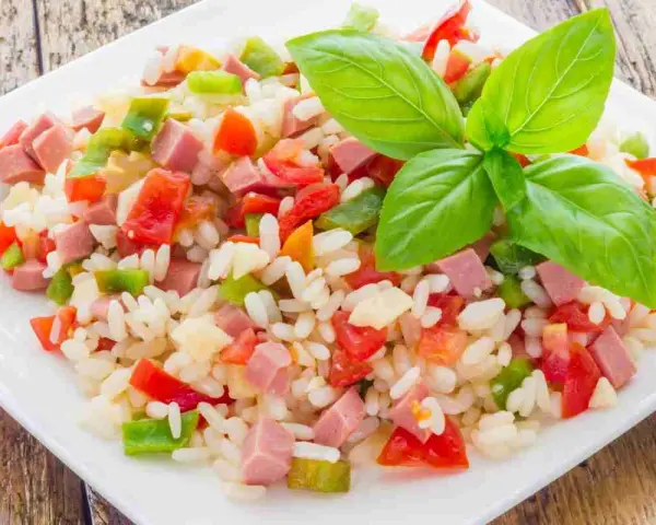 Un colorato insalata di riso con cubetti di prosciutto, peperoni e pomodori, guarnita con foglie di basilico fresco.