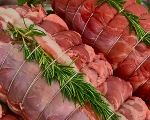Due **tagli di carne per arrosto** pronti per essere cucinati, legati con spago e guarniti con rametti di rosmarino fresco.