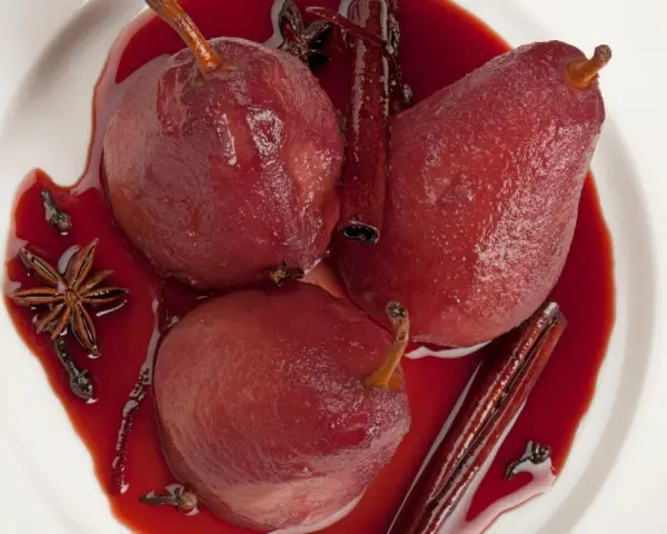 Pere cotte nel vino, profumate con cannella, anice stellato e chiodi di garofano, servite in una ciotola bianca.