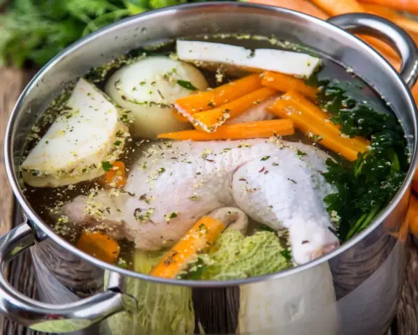 Brodo di pollo in pentola a pressione con carote, cipolla, sedano e prezzemolo.