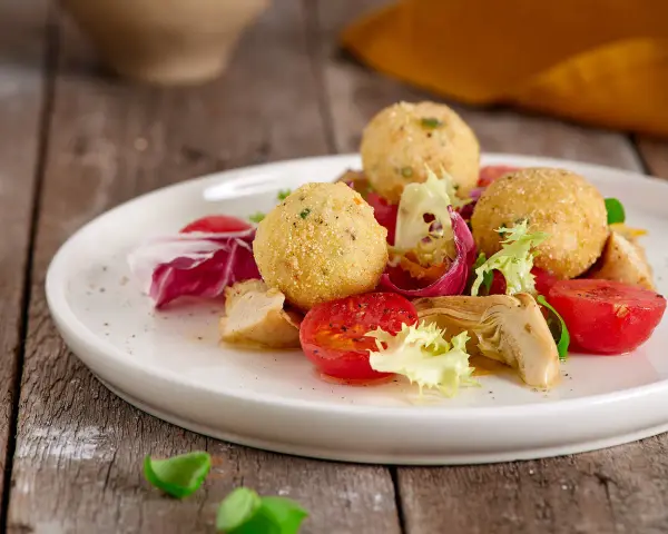 Sfere dorate di miglio fritte, servite con un'insalata fresca di pomodorini, radicchio e pollo. Un'idea gustosa per le tue ricette con miglio.