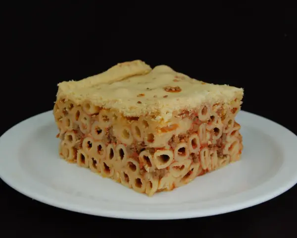 Un pezzo di timballo di pasta con ragù e pasta cotta al forno, servito su un piatto bianco.