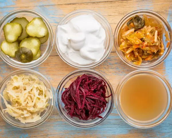 Sei ciotole di vetro con cetrioli, yogurt, kimchi, crauti, barbabietole e brodo, ingredienti per probiotici naturali fatti in casa.