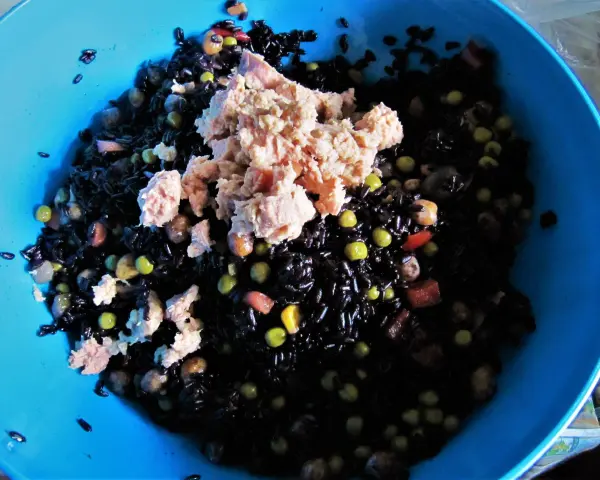 Un'insalata di riso nero con tonno, piselli e cubetti di pomodoro. La cottura del riso nero è perfetta, ogni chicco è ben separato.
