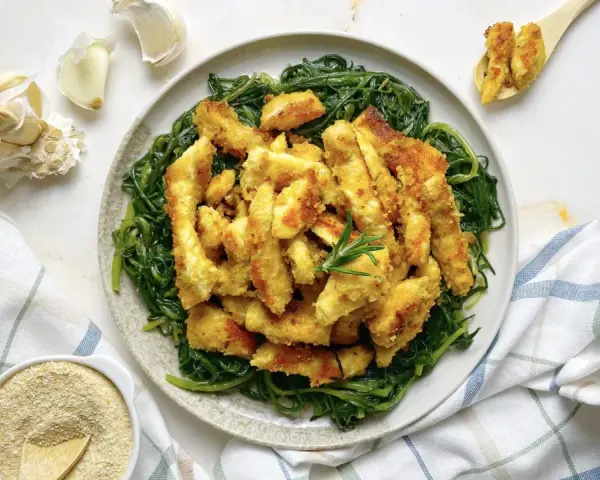 Luganega al forno croccante su letto di verdure verdi. Accanto, aglio e pangrattato.