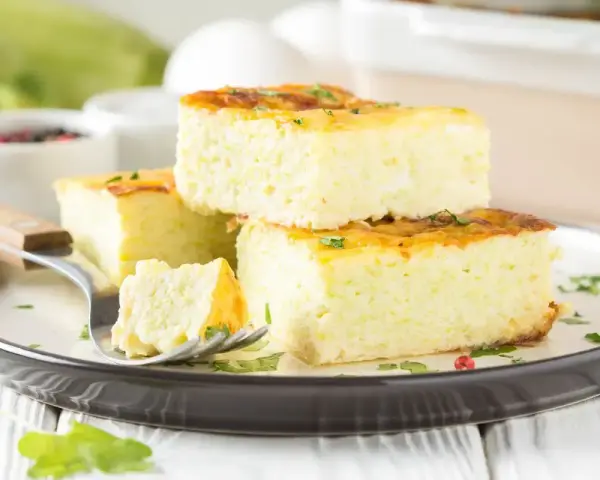 Fetta di frittata al forno soffice e alta, guarnita con erbe aromatiche, su un piatto scuro.