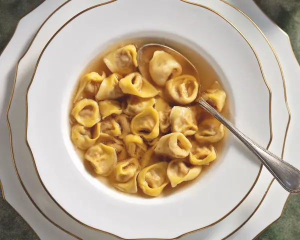 Un primo piatto fumante: tortellini in brodo, un classico della tradizione culinaria italiana, serviti in una ciotola bianca con bordo dorato.