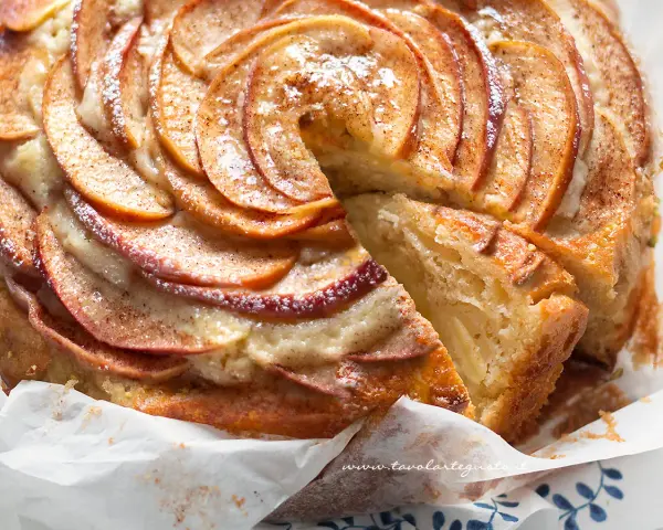 Una fetta di torta di mele e yogurt soffice, con mele a spirale e spolverata di cannella.