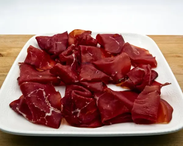 Fette di bresaola, la bresaola che carne è, su un piatto bianco.