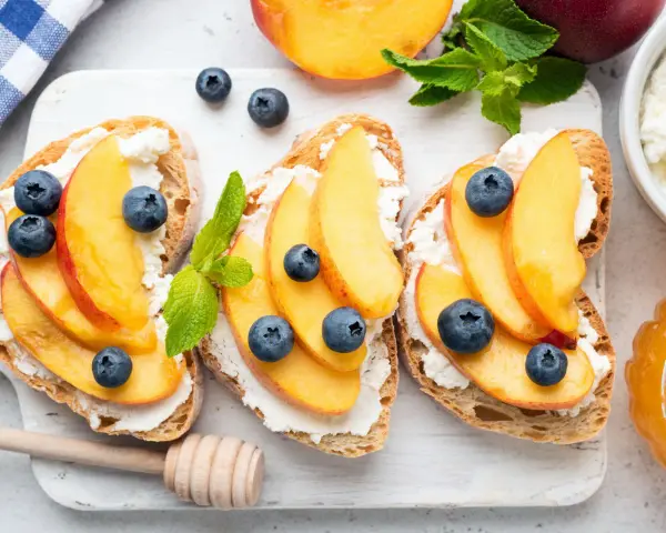 Bruschette con pesche mature, ricotta e mirtilli. Un'idea fresca per ricette con pesche mature, perfetta per la colazione o uno spuntino leggero.