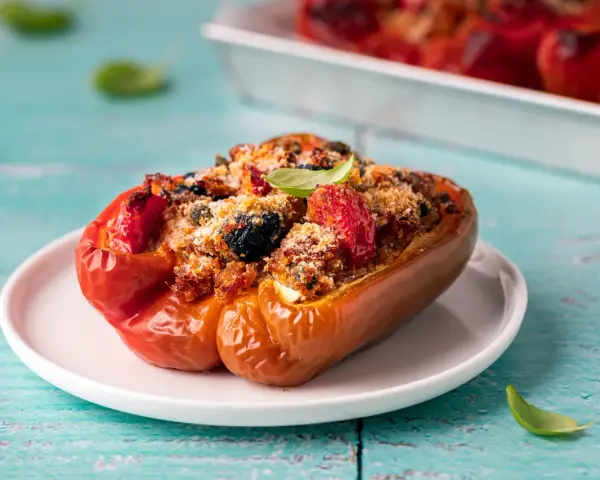 Peperoni ripieni, un classico delle ricette con peperoni, con un gustoso ripieno di pomodoro, olive e pangrattato, guarniti con basilico fresco.