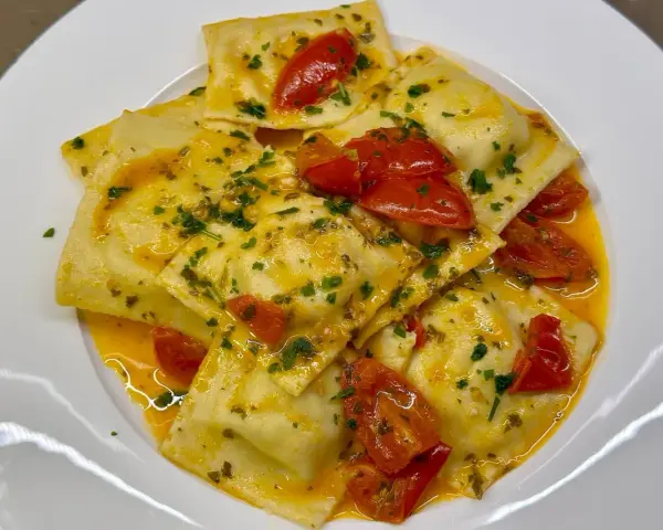 Deliziosi ravioli di pesce conditi con pomodorini e prezzemolo, in un sugo dorato.