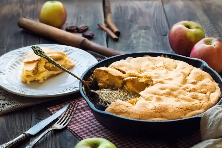Torta di mele in padella in 10 minuti: soffice e dorata, pronta per essere gustata. Una fetta invitante su un piatto bianco.
