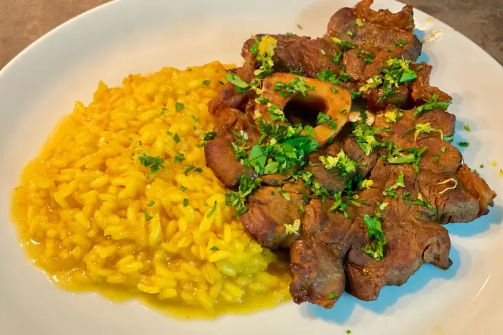 Un piatto invitante di risotto giallo cremoso accanto a un ossobuco tenero, guarnito con prezzemolo fresco e scorza di limone.