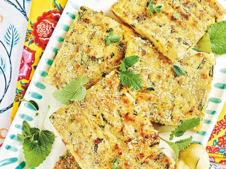 Fette dorate di polpettone di fagiolini, guarnite con erbe aromatiche fresche, su un piatto decorato con motivi floreali vivaci.