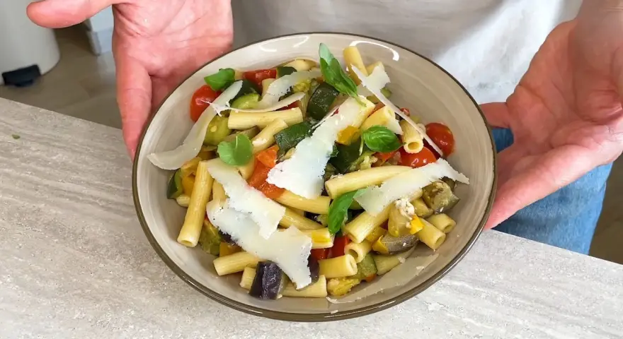 Un piatto di pasta fredda gourmet con verdure miste, pomodorini, basilico e scaglie di parmigiano.