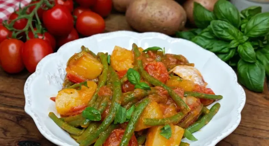 Un piatto di fagiolini e patate alla pugliese, con pomodorini freschi e basilico, pronto per essere gustato.