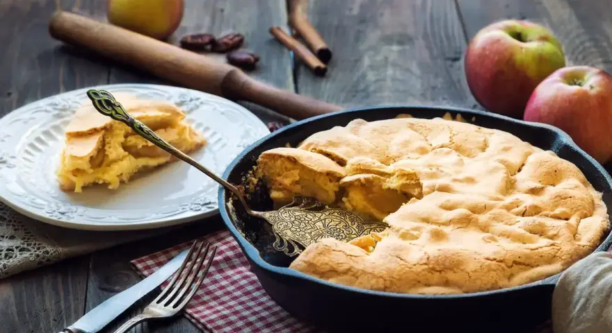 Torta di mele in padella in 10 minuti: soffice e dorata, pronta per essere gustata. Una fetta invitante su un piatto bianco.