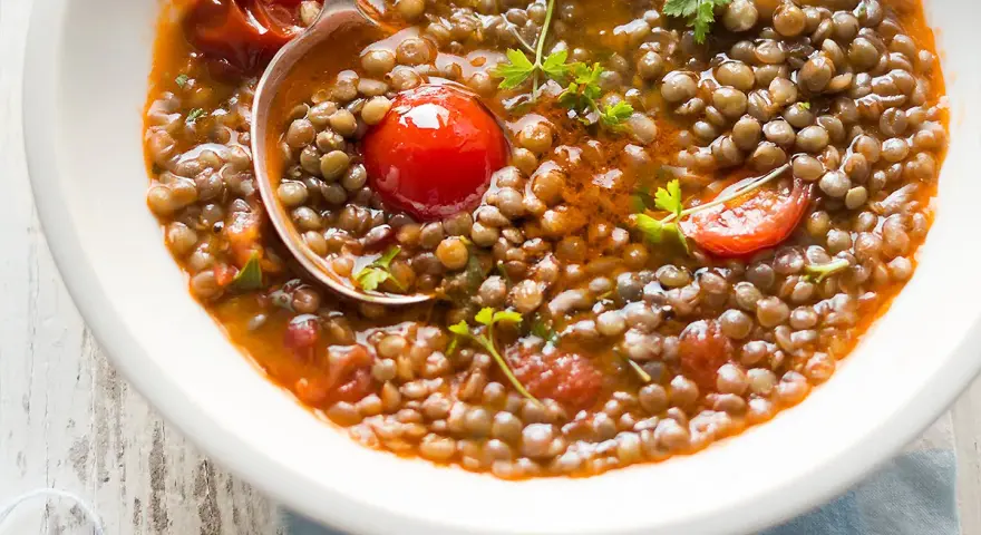 Una ciotola di zuppa di lenticchie veloce con pomodorini e prezzemolo fresco. Un cucchiaio serve la gustosa zuppa.
