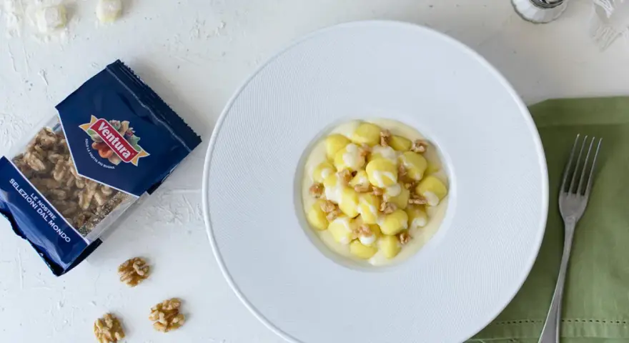 Gnocchi al Castelmagno con noci croccanti, un piatto cremoso e saporito. La confezione di noci Ventura accanto promette un tocco di gusto in più.