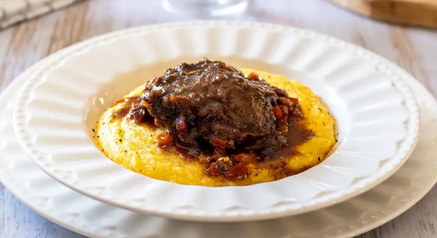 Guancette di maiale brasate su un letto di polenta cremosa, un piatto ricco e saporito.