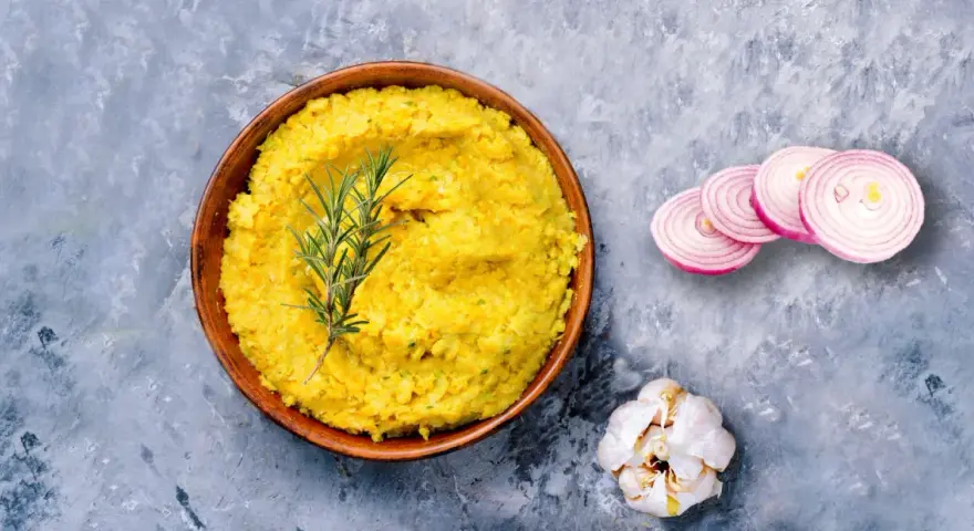 Piatto di lenticchie decorticate cremose, guarnito con rosmarino, cipolla rossa affettata e aglio.