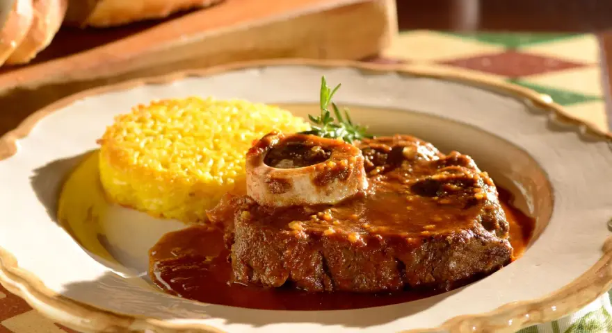 Un succulento ossobuco alla milanese, cotto lentamente e servito con polenta gialla e un rametto di rosmarino.