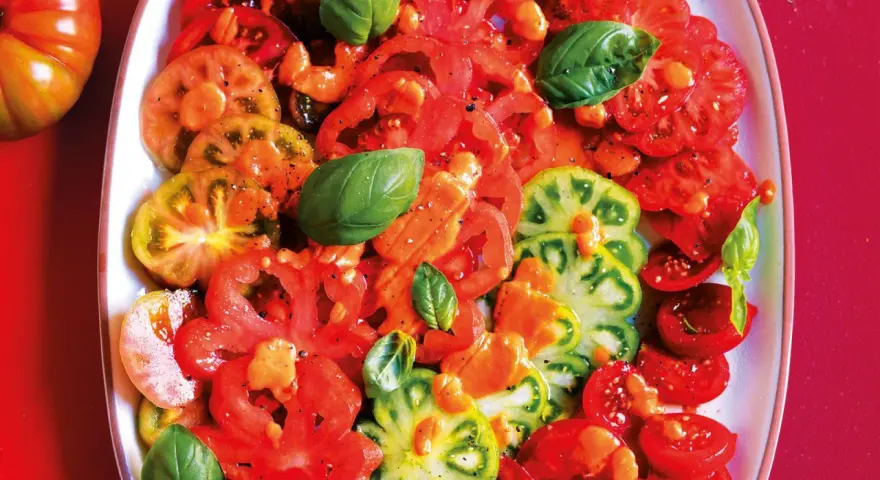 Un colorato carpaccio di pomodoro, con fette di diverse varietà, condito con olio e basilico fresco.