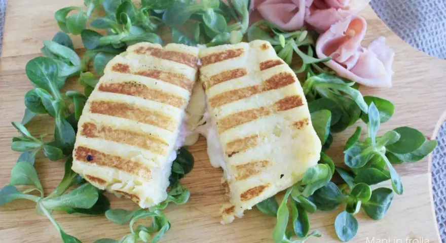 Toast di patate grigliato, ripieno di prosciutto e formaggio filante, servito su un letto di insalata fresca.
