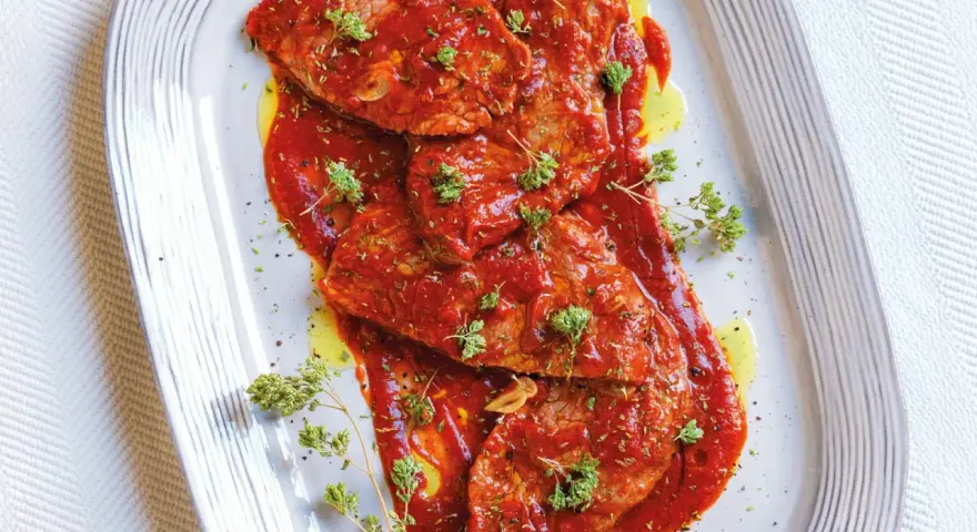 Bistecche alla pizzaiola succulente, ricoperte da salsa rossa e guarnite con erbe aromatiche fresche.