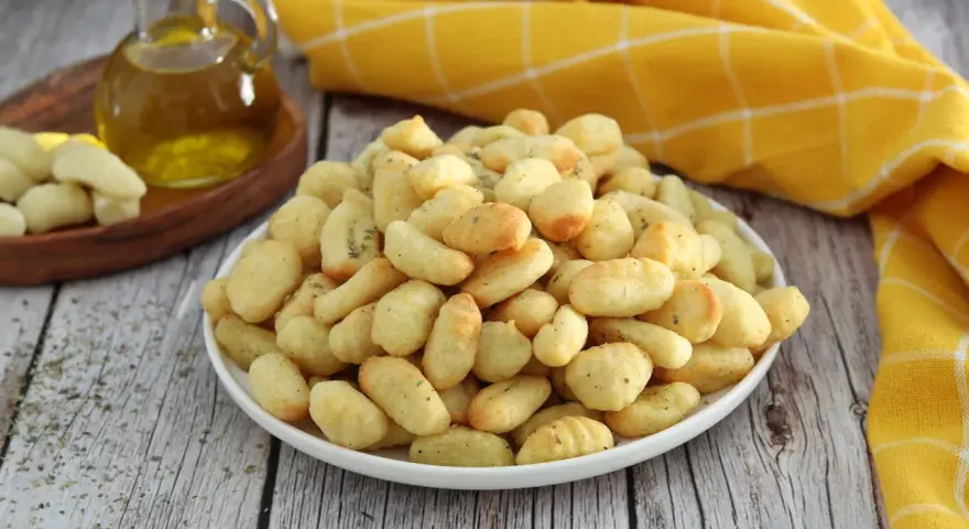 Gnocchi dorati e croccanti, cotti nella friggitrice ad aria, conditi con erbe aromatiche. Accanto, olio d'oliva e gnocchi crudi.