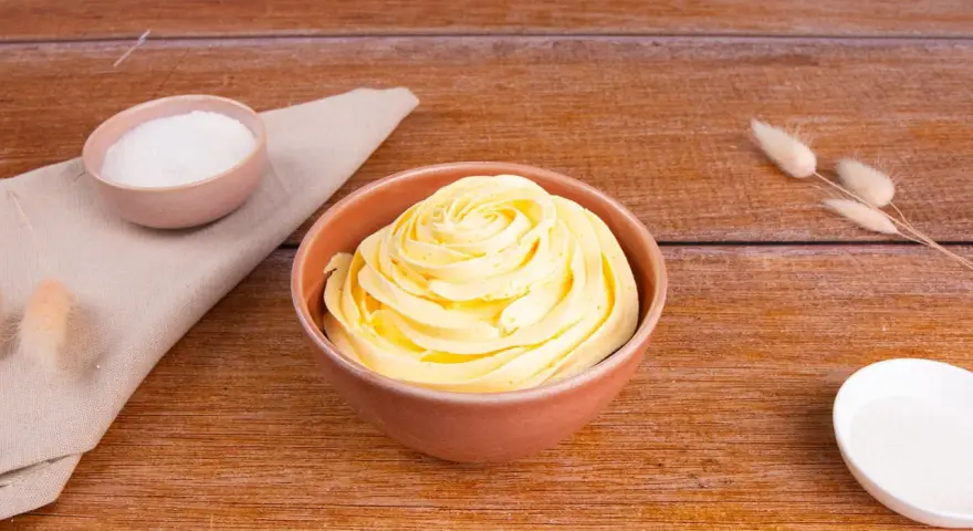 Crema al burro ricetta della nonna, soffice e profumata, pronta per decorare torte. Zucchero e ingredienti in vista.