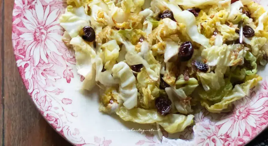 Deliziosa insalata di verza con uvetta, servita su un piatto decorato con fiori rossi.