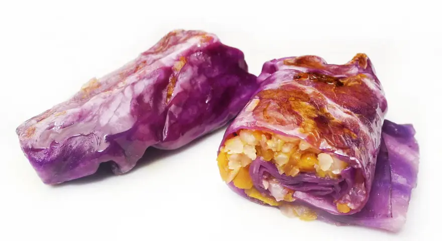 Due involtini di cavolo cappuccio viola, ripieni di riso e verdure, su sfondo bianco.