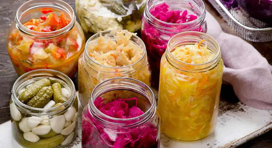 Vasi di vetro pieni di cibi fermentati fatti in casa: crauti, cavolo rosso, cetriolini e verdure miste.